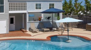 Exterior view of property with light gray shake siding and white trim, patio, pool, and patio furniture